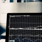 A computer screen displaying various line graphs and charts, possibly related to financial data or analytics, with a blurred office background.