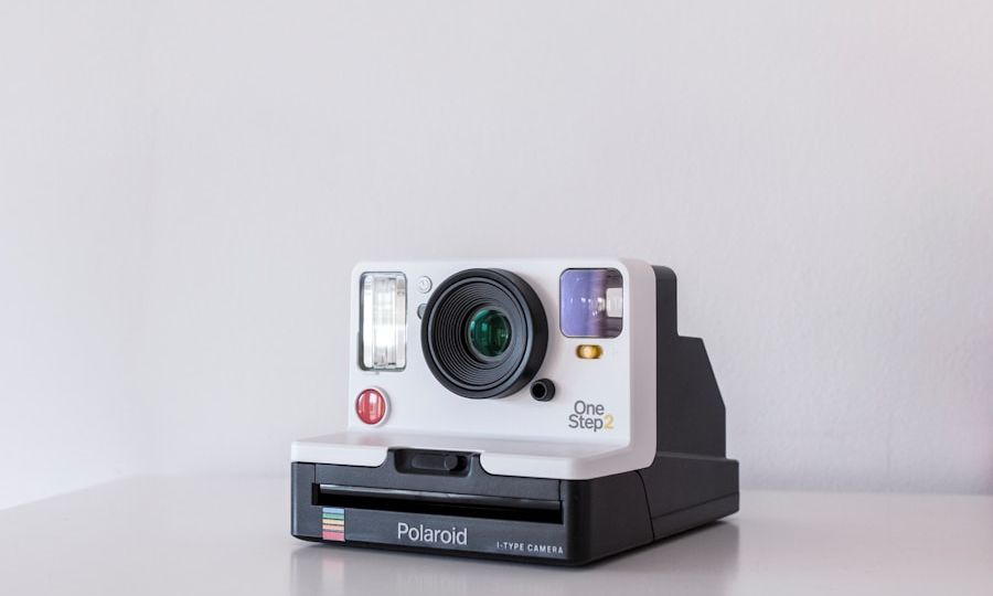 A vintage-style Polaroid OneStep 2 instant camera in white and black sits on a white surface against a plain background. The camera features visible lens, flash, red shutter button, and rainbow detail.